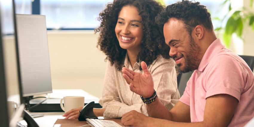 A colleague with Down syndrome explains something to his colleague on the computer.