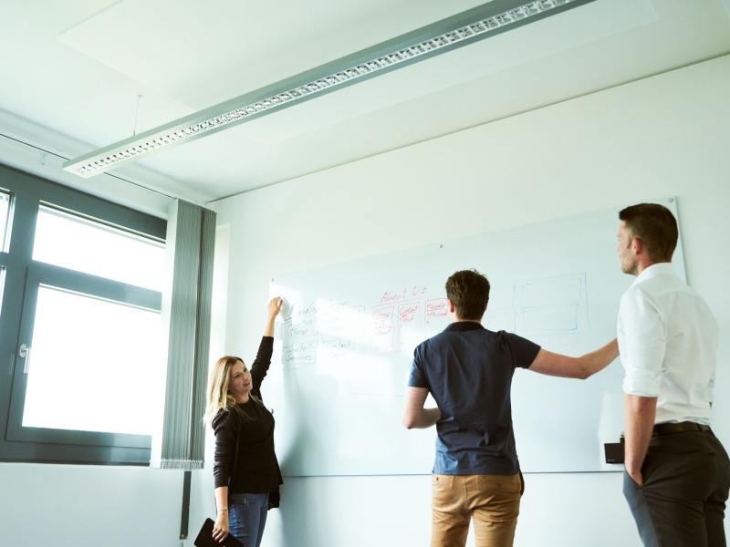 Eine Frau und zwei Männer stehen vor einem Whiteboard und zeichnen einen Verlauf Eine Frau und zwei Männer stehen vor einem Whiteboard und zeichnen einen Verlauf
