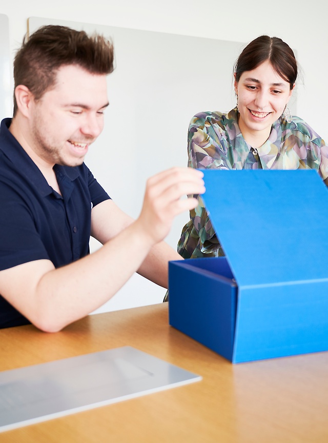 Mitarbeitende an einem Schreibtsich öffenen ein blaues Paket