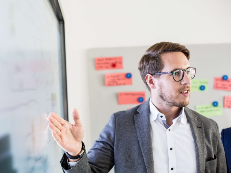 A man is standing infront of a whiteboard and is presenting something