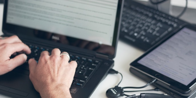 Hands typing on a laptop and a headset next to it.