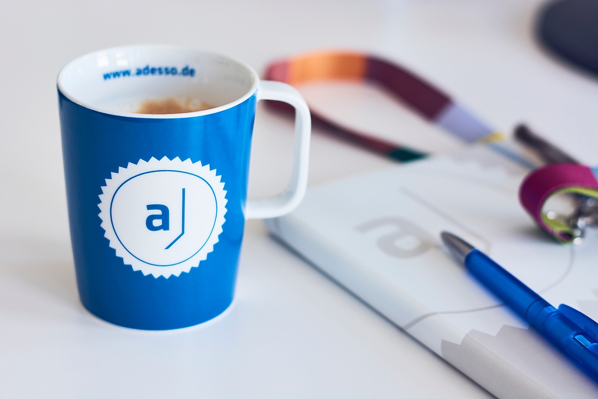 adesso-Tasse, Stift und Schlüsselband auf einem Schreibtisch