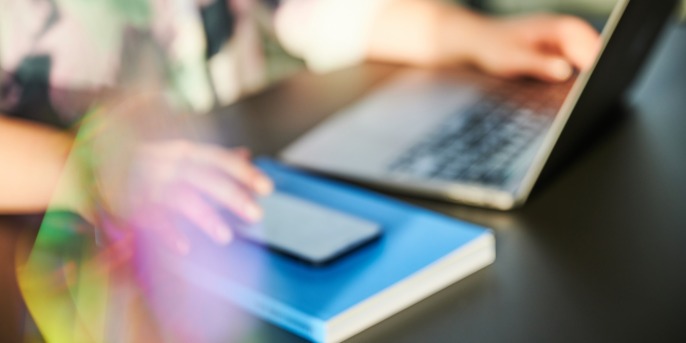 Person mit einer Hand am Laptop und einer Hand am Smartphone