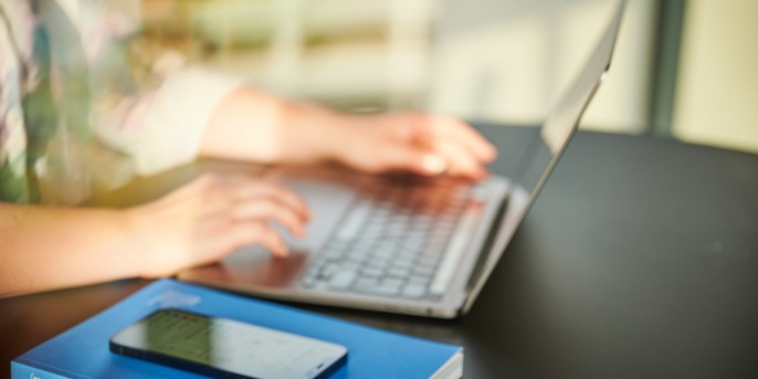 Person arbeitet am Laptop. Daneben liegt ein Smartphone