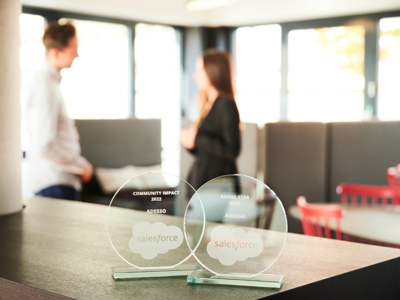 Salesforce Award stehen auf einem Tisch und im Hintergrund stehen zwei Personen